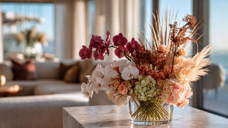Elegant autumn faux floral arrangement featuring burgundy orchids, blush hydrangeas, pampas grass, and soft peach roses in a glass vase by True Bloom Floral™