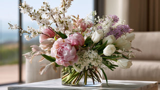 Elegant faux spring floral arrangement featuring blush peonies, white tulips, lilacs, and cherry blossoms styled in a modern glass vase by True Bloom Floral™