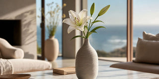 Single white lily stem in a narrow neck ceramic vase styled on a marble table in a bright modern living room