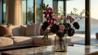 Dark burgundy and black faux floral arrangement in a ribbed glass vase on a marble table, styled in a modern luxury living room with soft neutral tones