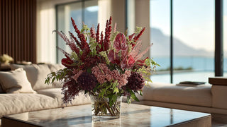 Burgundy and deep red faux floral arrangement with anthurium and dahlias in a glass vase, styled on a marble table in a luxury modern living room