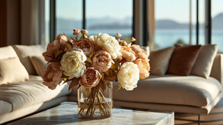 Taupe and neutral peony faux floral arrangement in a glass vase on a marble coffee table, styled in a modern coastal living room with warm natural light and ocean view
