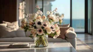 Luxury faux blush and white anemone floral arrangement in a clear glass vase on a marble coffee table, styled in a bright coastal living room with ocean view and soft natural sunlight, modern elegant home decor