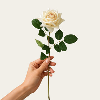 Held in woman's hand pale yellow True Bloom Real Touch Duchess Rose Stem with layered garden rose petals and realistic foliage; pairs beautifully with white peonies, peach anemones, hydrangeas, and eucalyptus because the soft yellow coloring brightens arrangements while maintaining a sophisticated, balanced look across every season including holiday styling.