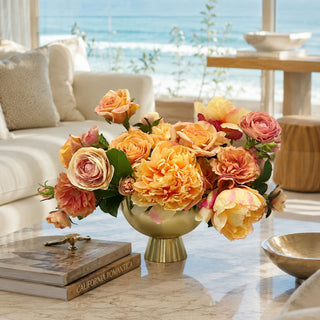 Apricot Garden artificial premade floral arrangement styled in a metal gold vase on a marble coffee table with apricot roses, peach peony-style blooms, cream florals, blush accents, and green foliage in a bright coastal living room.