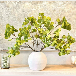 Artificial green aspen branches styled in a white ceramic vase creating a realistic faux botanical arrangement in a luxury modern home.