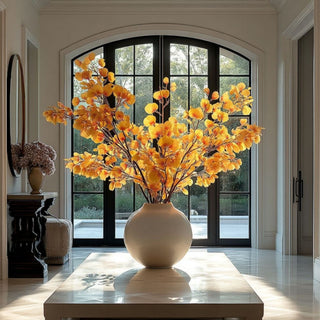 Artificial yellow aspen branches styled in a white vase creating a luxury fall arrangement with realistic faux golden foliage in a modern entryway.