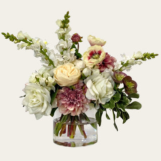 Blush Garden Manor premade True Bloom Real Touch floral arrangement shown in a clear glass vase with cream roses, white florals, blush and mauve blooms, soft burgundy accents, and green foliage for year-round coffee table, entry console, kitchen island, and dining table styling.