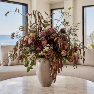 Brown and Green Leucaena Glauca Stem styled in a tall stone vase with burgundy dahlias, mauve roses, dried-style filler, fern greenery, and layered fall foliage in a bright coastal living room arrangement.
