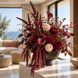 Burgundy faux amaranthus stems cascading from a large seasonal arrangement with burgundy, blush, and plum flowers in a dark pedestal vase.