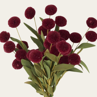 Close-up of burgundy fuzzy pom-pom flowers with EVA green leaves, showing the soft polyester-style texture, rounded shape, and faux foliage detail.