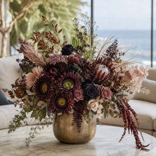 Burgundy Real Touch Sunflower Bundle of 6 stems styled as focal flowers in a fall arrangement with black roses, mauve roses, mink protea, burgundy amaranthus, pampas grass, eucalyptus, and layered seasonal greenery in a brass vase on a marble coffee table.