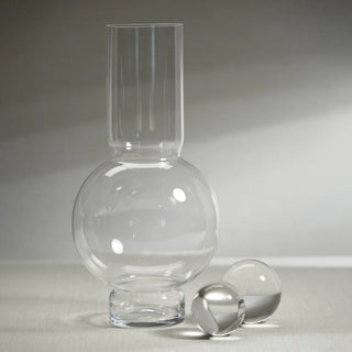 Clear Monceau Glass Vase shown in a studio setting with a sculptural rounded base and tall neck, ideal for creating structured faux floral arrangements with tulips, roses, greenery, branches, and seasonal stems.