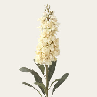 Close-up of cream polyester stock blossoms with layered clustered petals, smaller upper buds and muted green PE foliage on a traditional faux floral stem.