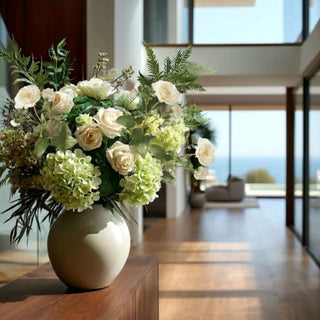 Cream True Bloom Real Touch Distant Drum rose stems styled in a large entryway arrangement with green hydrangeas, soft fern greenery, airy white filler, and layered foliage in a neutral vase.