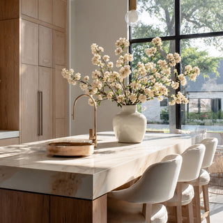 Creamy white True Bloom real touch blossom branches styled in a white ceramic vase on a marble kitchen island in a bright modern kitchen with warm wood cabinetry