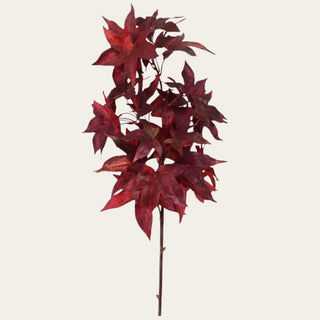 Close-up of crimson red faux maple leaves showing deep seasonal color, pointed leaf shapes, visible veining, and layered foliage on a flexible branch.