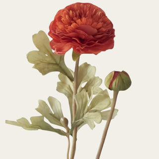 Close-up of dark orange artificial ranunculus with layered polyester petals, unopened green and orange bud, and soft sage-green Traditional Faux leaves.
