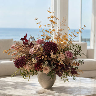 Dark Yellow Eucalyptus Stem styled as tall movement greenery in a fall floral arrangement with burgundy hydrangeas, mauve roses, cream filler flowers, burgundy foliage, and layered seasonal greenery in a stone vase on a marble coffee table in a bright coastal living room.