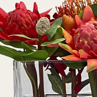 Close up view of the Ember Reserve faux floral premade arrangement shown in a clear rectangular glass vase with red, ember orange, coral, rust, and green faux florals for low-profile dining table, coffee table, kitchen island, and console styling.