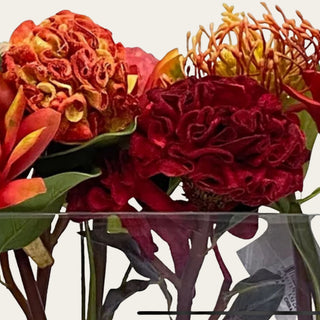 Close up view of the Ember Reserve faux floral premade arrangement shown in a clear rectangular glass vase with red, ember orange, coral, rust, and green faux florals for low-profile dining table, coffee table, kitchen island, and console styling.