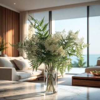 Faux greenery and filler stems arrangement in a clear glass vase on a marble coffee table, styled in a bright coastal living room with soft natural light