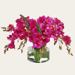 Fuchsia Conservatory faux floral premade arrangement shown in a clear glass vase with vivid fuchsia orchid-style blooms, green leaves, and arched faux stems for coffee table, kitchen island, entry console, sideboard, and dining table styling.