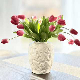 Fuchsia True Bloom real touch tulips arranged in a white textured ceramic vase with soft green leaves and naturally curved stems for a bright faux floral centerpiece.
