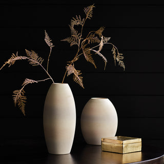 Gilded artificial fern stems arranged in a tall white statement vase, showing airy sculptural movement for year-round and holiday styling.