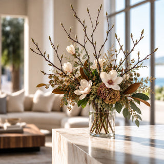 Tall green Real Touch magnolia bud branches styled with white magnolia flowers, hydrangeas, berries, and foliage in a clear glass vase.