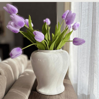Light purple True Bloom real touch tulip stems styled in a glossy white vase with long green leaves beside a window in a softly lit living room