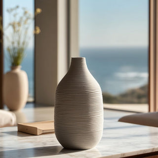 Narrow neck white ceramic vase with ribbed texture on a marble table, styled in a minimalist modern living room with coastal view