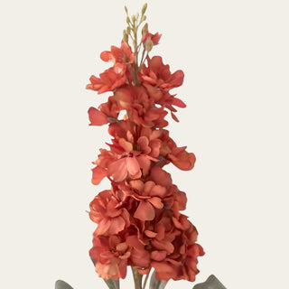 Close-up of orange artificial stock flowers with layered polyester petals, terracotta and coral-orange tones, smaller blossoms and unopened buds.