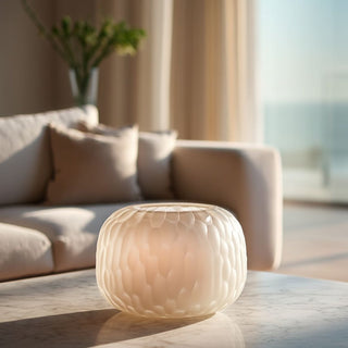 Small white textured glass vase on a marble coffee table, styled as a petite decorative accent in a bright modern living room with soft neutral tones