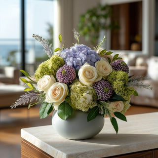 Purple Real Touch Sedum stems arranged with blue hydrangeas, green hydrangeas, ivory roses, and greenery in a modern ceramic vase, showcasing layered texture, soft movement, and year-round floral styling for coastal, transitional, and contemporary home décor.
