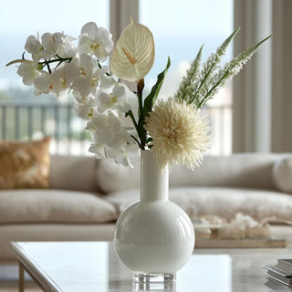 33 Inch White real touch orchid stem arranged with other creamy and white colored floral stems in a glossy white glass vase on a marble table of a luxury home 