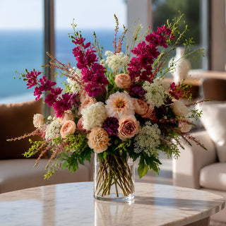 Fuchsia true bloom real touch delphinium stem styled in a large floral arrangement in a glass vase on a marble coffee table in a modern coastal home with ocean views