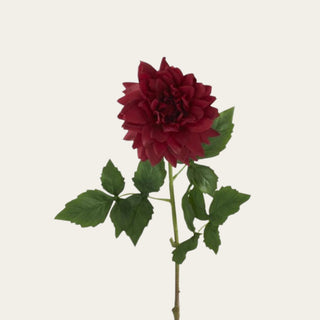 Close-up of red real touch dahlia bloom showing layered petals, saturated red color, and a soft floral surface with traditional faux green leaf detail.
