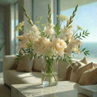Step Four adding filler of parsley fern to white tulips, creamy peony and white gladiolus stems, styled in a clear glass vase on a marble table in a modern coastal home