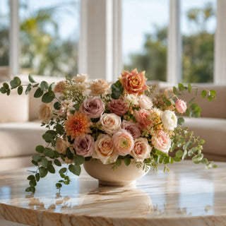 Luxury faux floral arrangement by True Bloom Floral featuring apricot Duchess roses, blush spray roses, creamy white blooms, airy greenery, and soft peach accents arranged in a neutral ceramic vase on a marble coffee table in a bright modern living room.