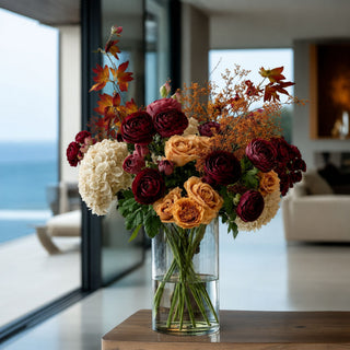 Burgundy True Bloom Ranunculus stems styled with pale yellow roses, white florals, and airy greenery in a luxury living room arrangement; works beautifully in spring, fall, and winter because the rich burgundy blooms create focal contrast while lighter flowers add balance and softness.