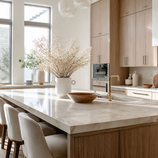 Large white ceramic loop handle vase styled with airy white branches on a marble kitchen island in a bright modern kitchen with light wood cabinetry