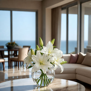 White Faux Casablanca Lily Premade Floral Arrangement styled in a clear glass vase with lifelike faux water on a wood coffee table, featuring sculptural white lily blooms and green buds for polished spring, summer, and everyday home décor.