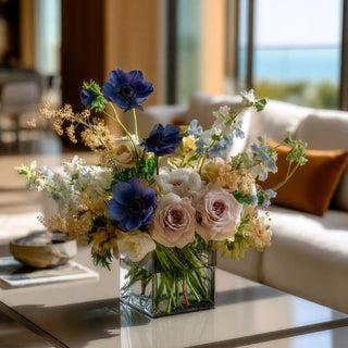 Styled in an arrangement, dark blue real touch 17.5 inch anemone stem with complementary florals in a clear glass vase on a marble table in a luxury coastal home.