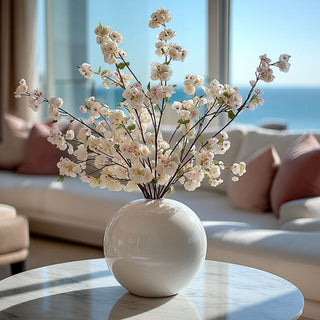 Creamy white true bloom real touch 23 inch blossom branch stem styled in a round glossy white glass vase on a marble coffee table in a luxury modern coastal home with neutral colored decor.