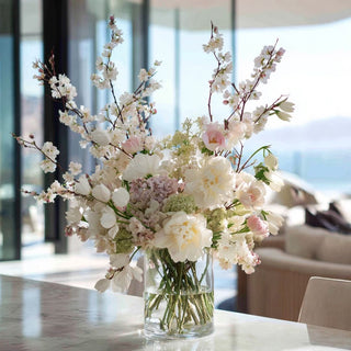 Styled cherry blossom stem arrangement with roses, peony and ranunculus in a clear vase on a marble counter in a california coastal home