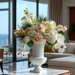 Glossy white 12 inch resin floral urn styled with a tropical inspired floral arrangement on a marble coffee table in a well decorated living room 