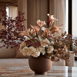 Styled artificial fall floral arrangement with burgundy Japanese maple, blush calla lilies, cream hydrangeas, and eucalyptus in a brown vase on a marble coffee table.