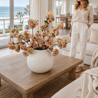 Light peach and linen True Bloom Real Touch blossom branches styled in a white rounded vase on a coffee table in a bright coastal living room, creating a soft statement arrangement with height, movement, and warm seasonal color.