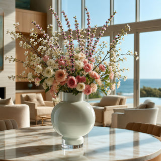 Luxury floral arrangement featuring pink confetti blossom branch stems and other florals to create a summer inspired arrangement. in a vase on a marble coffee table in a luxury coastal home with ocean views